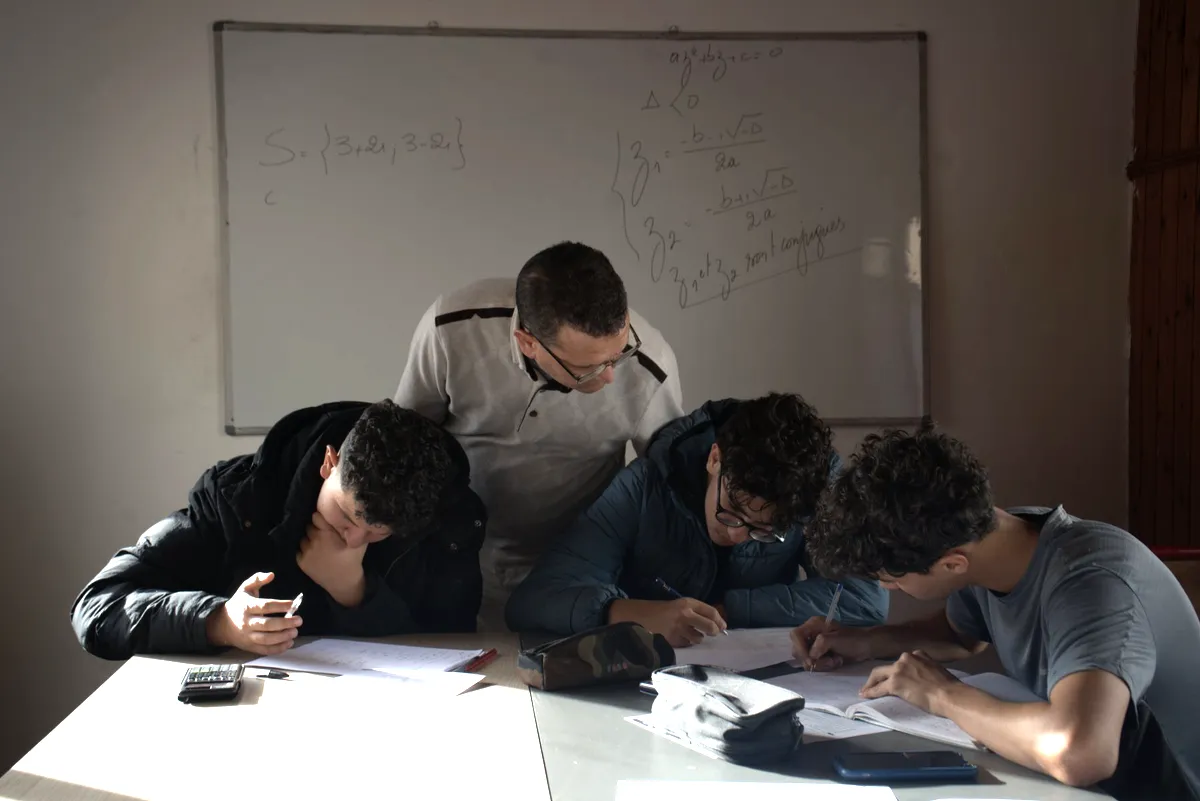 Un enseignant Cap Mission penché sur la table de travail d’un petit groupe d’élèves